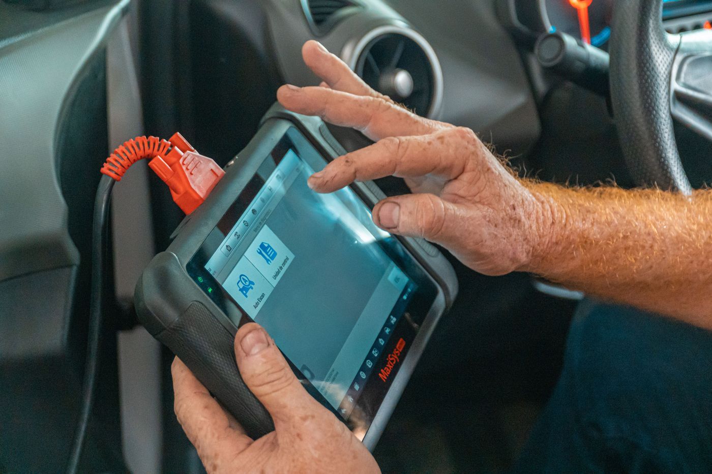 Technician's hands on a scan tablet connected to a vehicle's diagnostic port
