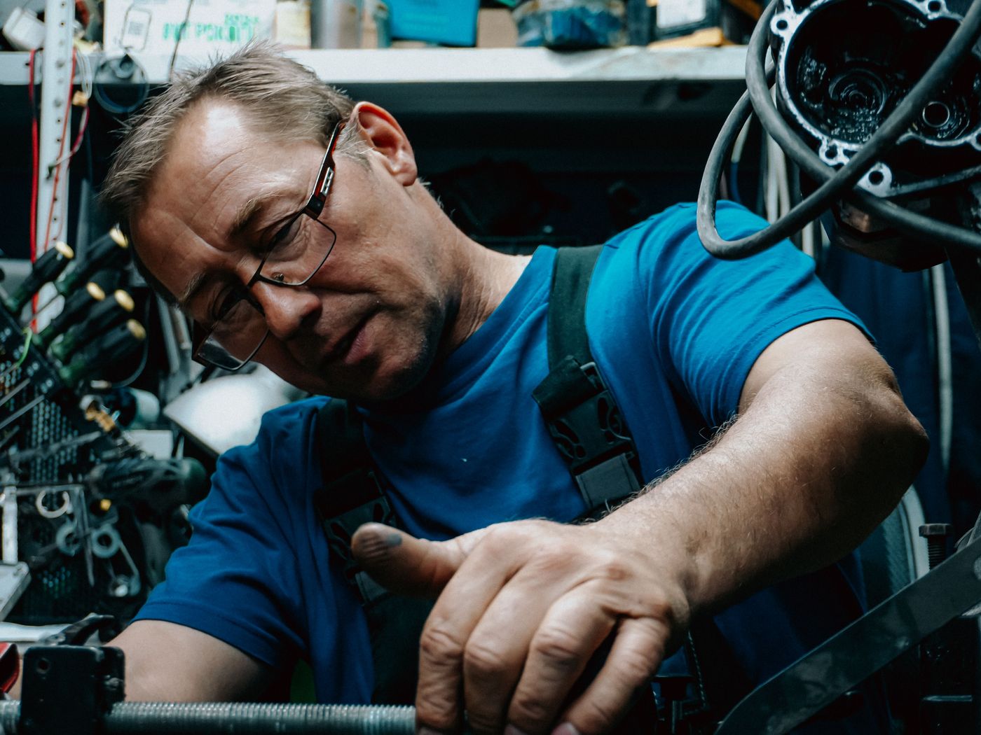 Mechanic in glasses working on engine parts in a busy shop